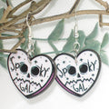 Heart-shaped earrings with 'Spooky Gal' text and skull design on a branch background