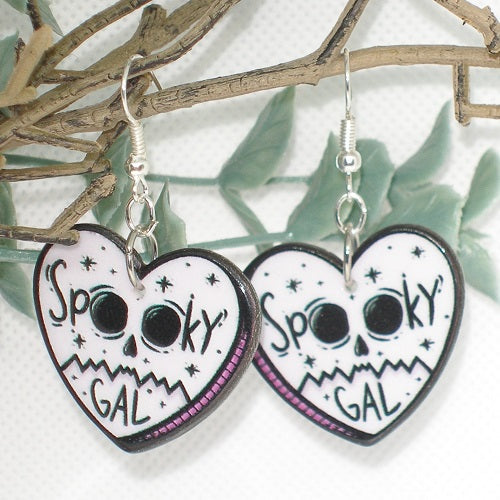 Heart-shaped earrings with 'Spooky Gal' text and skull design on a branch background