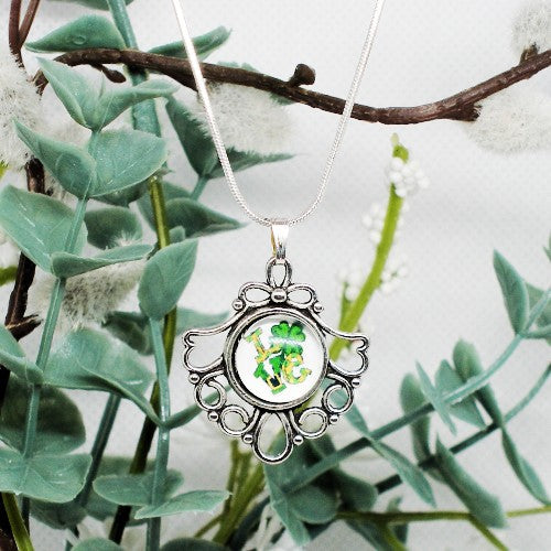 Silver pendant with green design on a branch with leaves