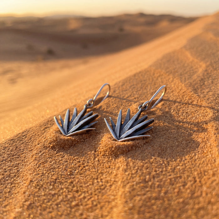 Silver leaf-shaped earrings on sand with a desert background