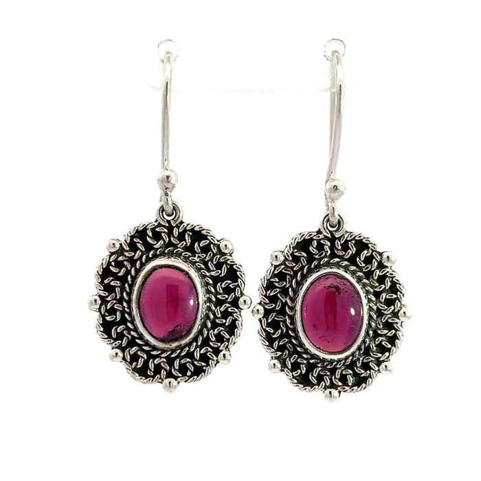 photo of a pair of oval silver filigree earrings set with an oval red garnet on a white background