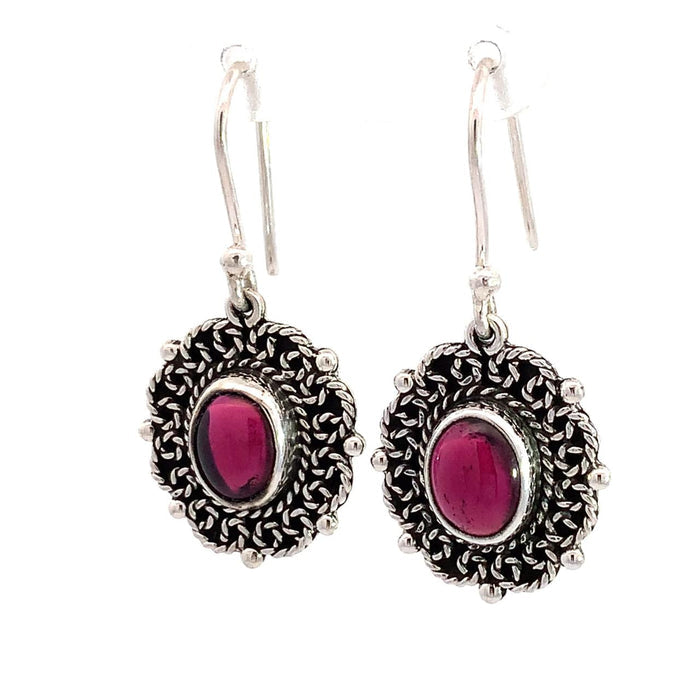 photo of a pair of oval silver filigree earrings set with an oval red garnet on a white background