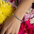 photo of a models arm wearing a silver cuff on a bed of flower petals