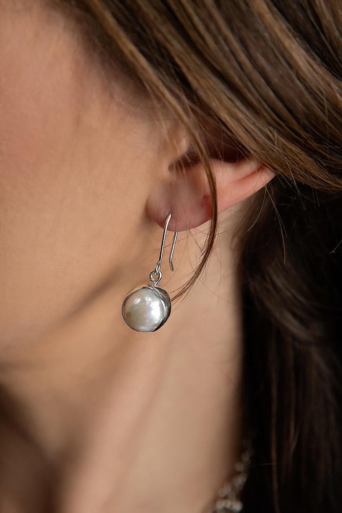 photo of a brunette model wearing a Taxco artisan sterling silver white mabe pearl dangle earrings handcrafted Mexican silver jewelry