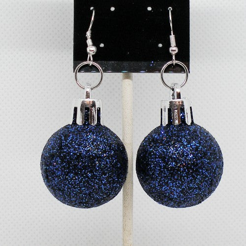 Blue glittery ball earrings on a black card against a light gray background