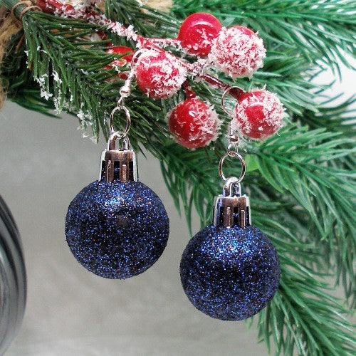 Blue glittery Christmas ball earrings on a green branch with red berries  background