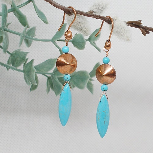 Pair of earrings with turquoise stones and copper accents on a branch with leaves.