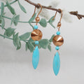 Pair of earrings with turquoise stones and copper accents on a branch with leaves.