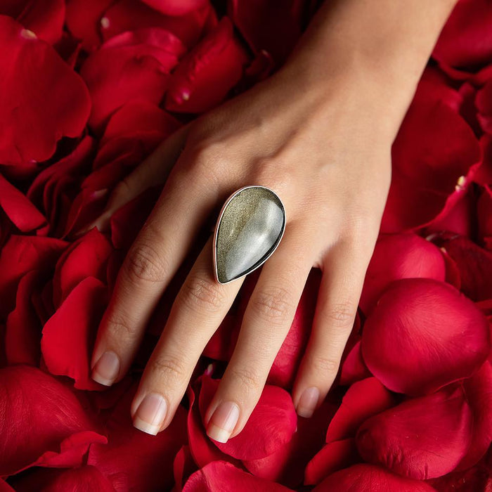 photo of a models hand wearing a large pear shape obsidian silver ing on a bed of rose petals