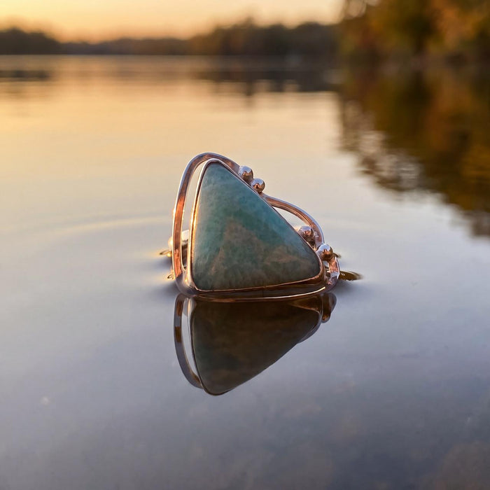 photo of a water background featuring silver ring set with a triangular light blue opaque gem