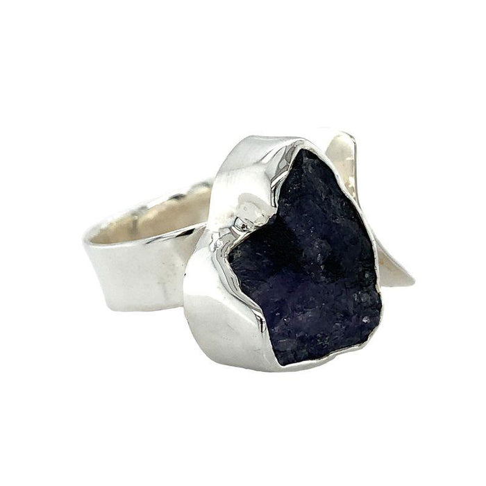 photo of a bold silver ring set with a raw irregularly shaped tanzanite on a white background front -side view