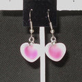 Heart-shaped earrings with pink and white design on a black card.