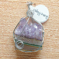Amethyst crystal pendant in a silver wire wrap on a textured surface