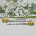 Silver hair pins with yellow circular ends on a white background with flowers.