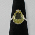 Ring with a pear-shaped yellow gemstone on a black stand against a gray background