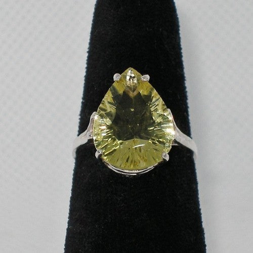 Ring with a pear-shaped yellow gemstone on a black stand against a gray background