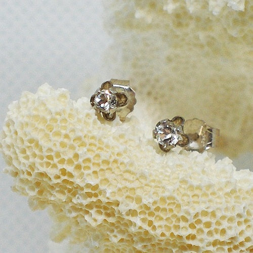 Gold stud earrings with clear gemstones on a coral background