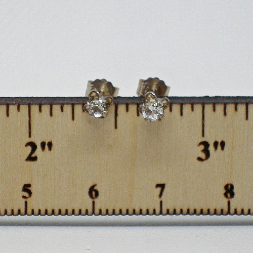 Pair of  white zircon stud earrings on a wooden ruler for scale.